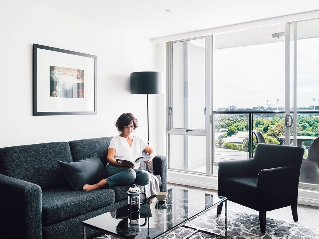 Lady reading a magazine in 1 Bedroom Deluxe Apartment lounge at Quay West Suites Melbourne