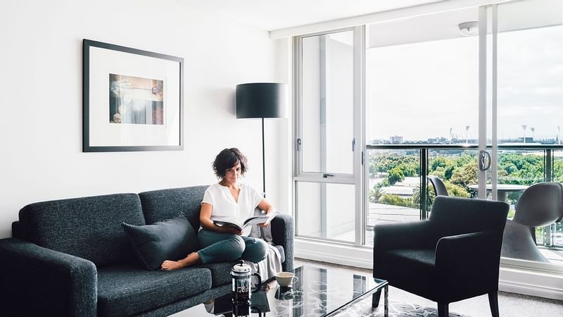 Lady reading a magazine in 1 Bedroom Deluxe Apartment lounge at Quay West Suites Melbourne