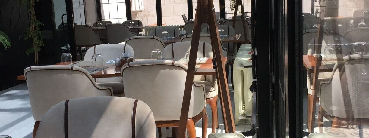 Dining chairs by wooden tables surrounding a tall tripod floor lamp in Maple Tree Restaurant at Warwick Ankara