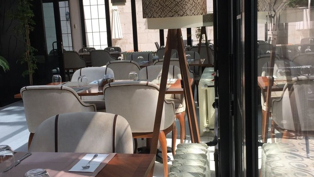 Dining chairs by wooden tables surrounding a tall tripod floor lamp in Maple Tree Restaurant at Warwick Ankara