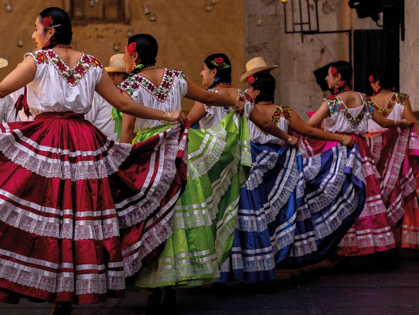 Mujeres con vestidos tradicionales coloridos realizando una danza en Camino Real Hotels