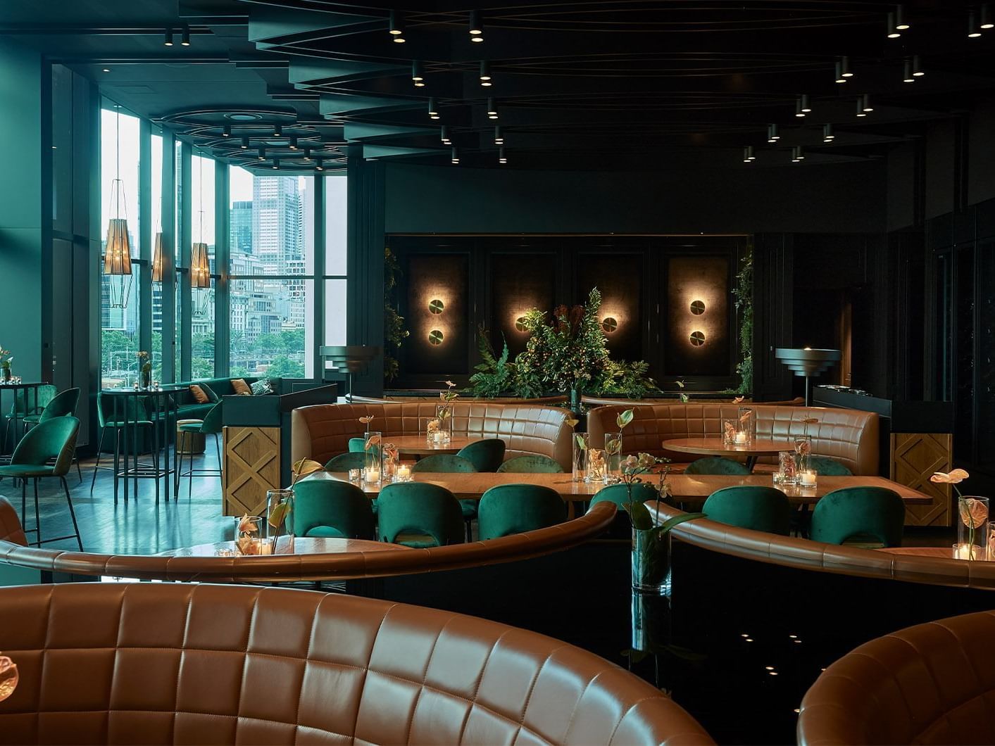 Restaurant interior with dark hues, green velvet chairs, leather booths, and city view at Crown Hotel Perth
