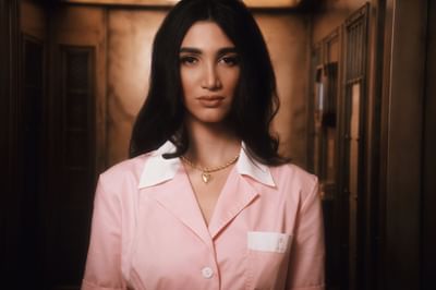 Woman in a pink uniform with a heart necklace, standing in a warmly lit elevator at Hotel Motto Vienna