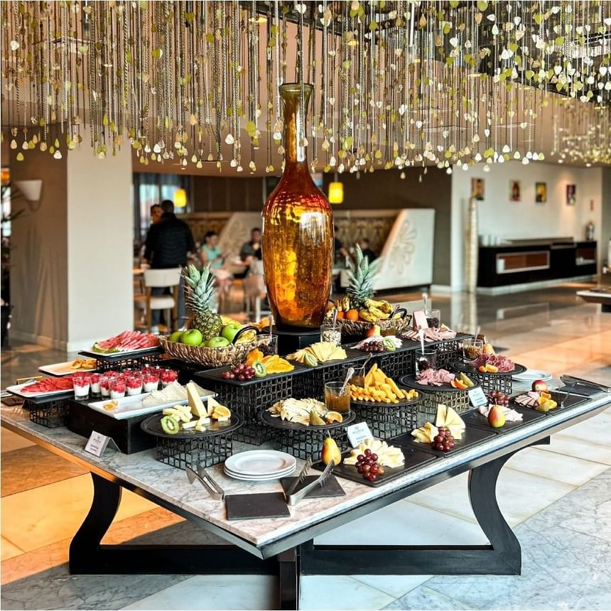 Bufé de desayuno con fruta fresca, queso y fiambres bajo lámparas colgantes en Megapolis Hotel Panama