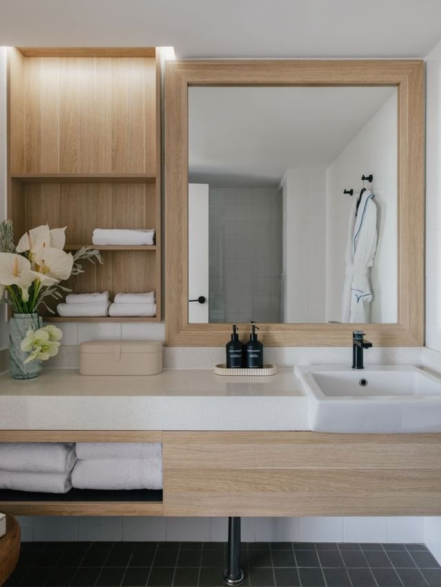 Atrium King at Elysium Manly with a wood-framed mirror, folded towels under a robe beside a vase of white flowers