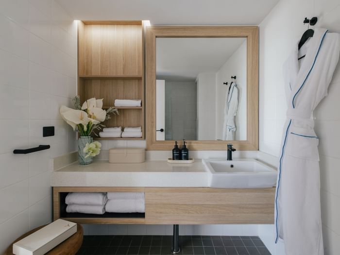 Atrium King at Elysium Manly with a wood-framed mirror, folded towels under a robe beside a vase of white flowers
