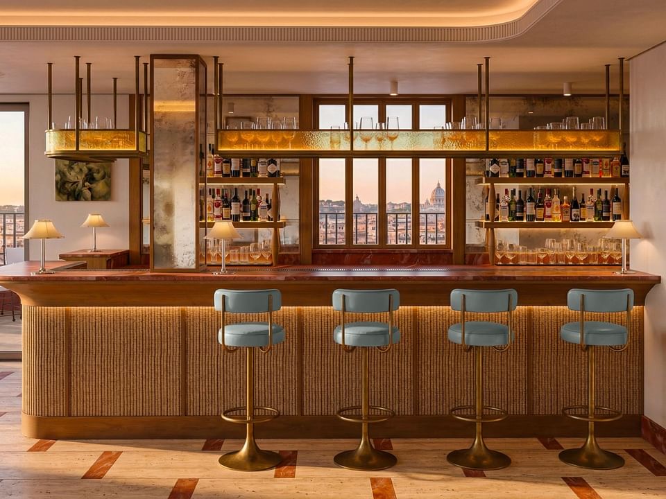 Leather bar stools lined along a wooden counter below shelf with liquor bottles & glasses in Lyve Restaurant at Thompson Rome