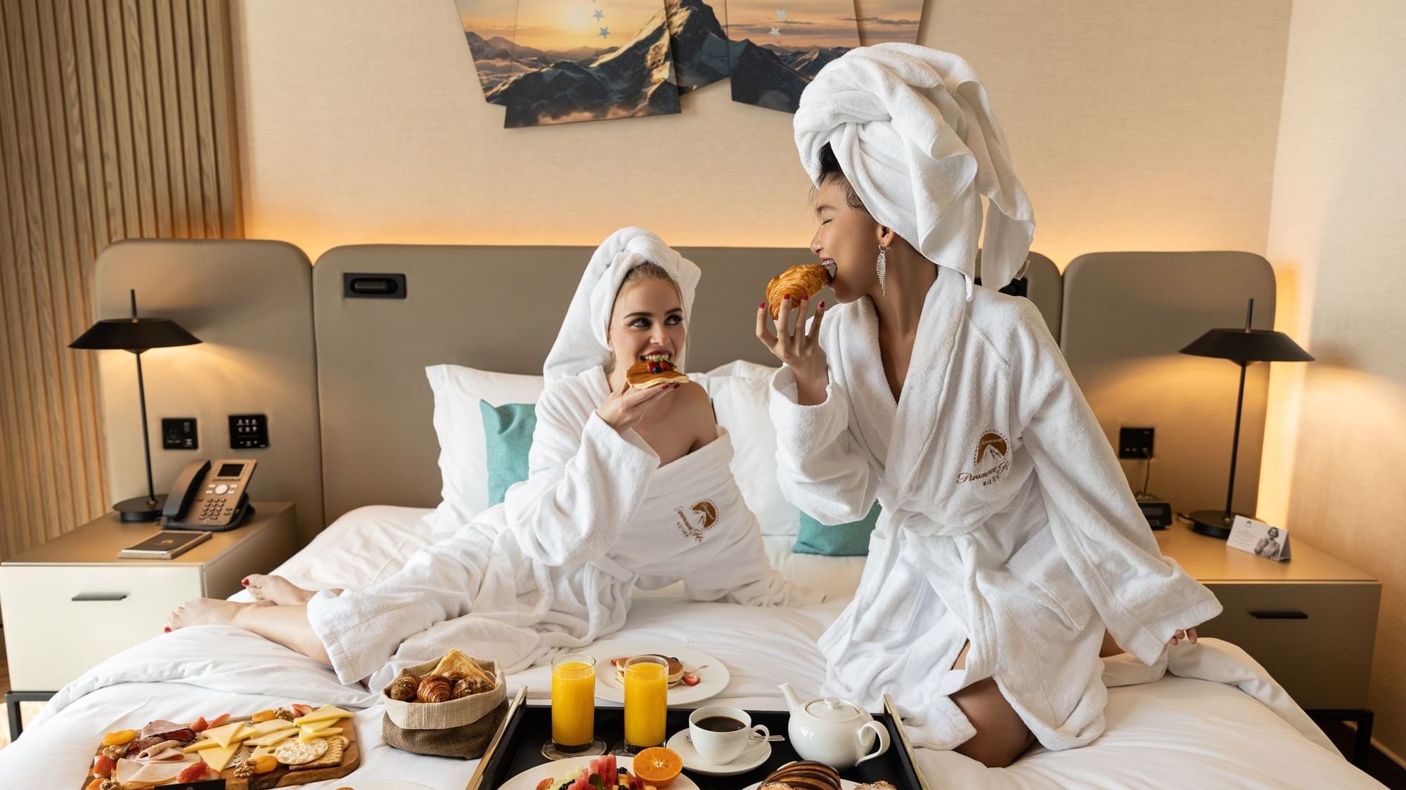 Two women in robes enjoying breakfast in Scene Room at Paramount Hotel Midtown, featuring a large, beautiful platter