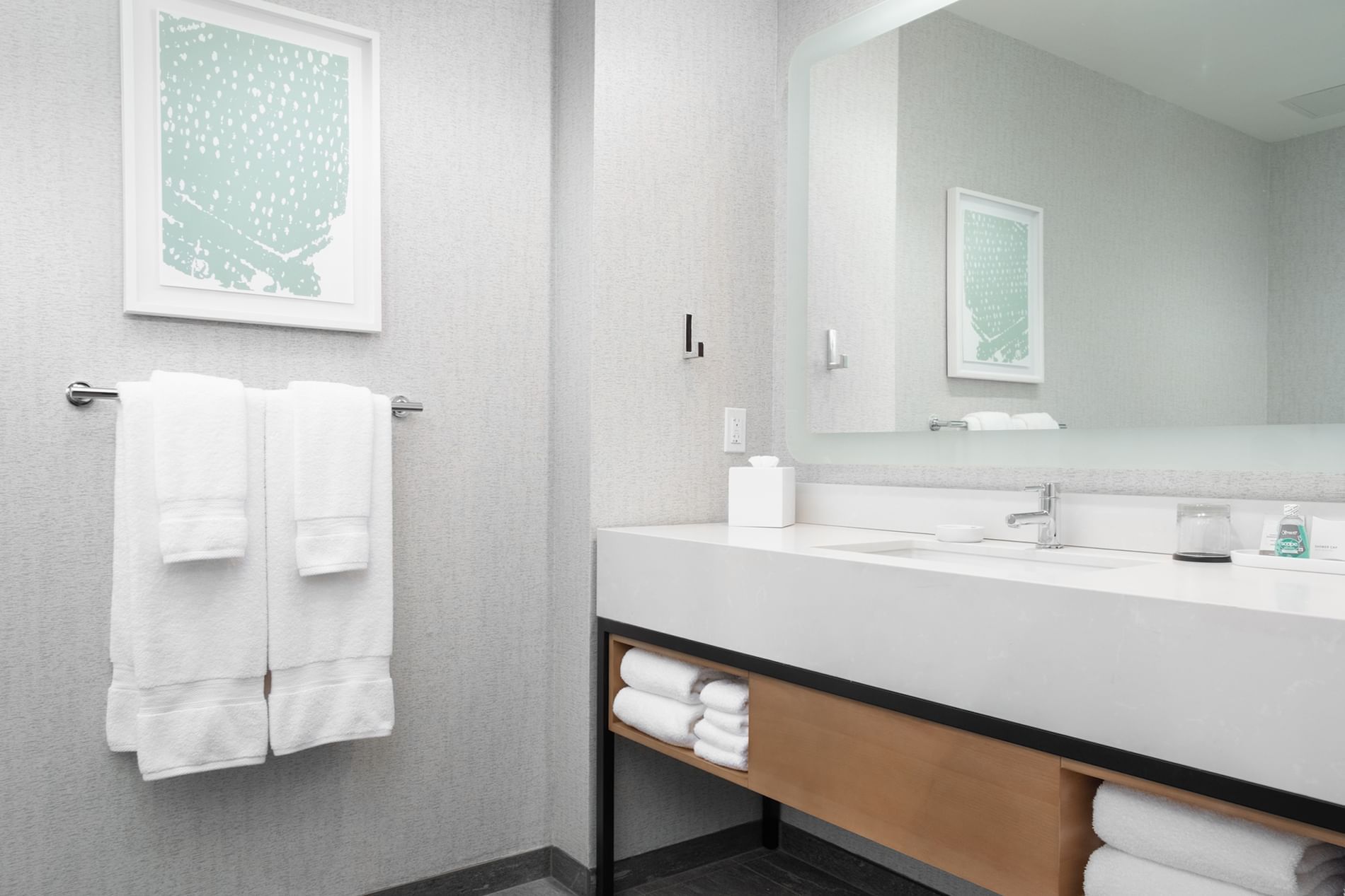 A clean and modern bathroom with a large mirror, a single sink, and white towels.