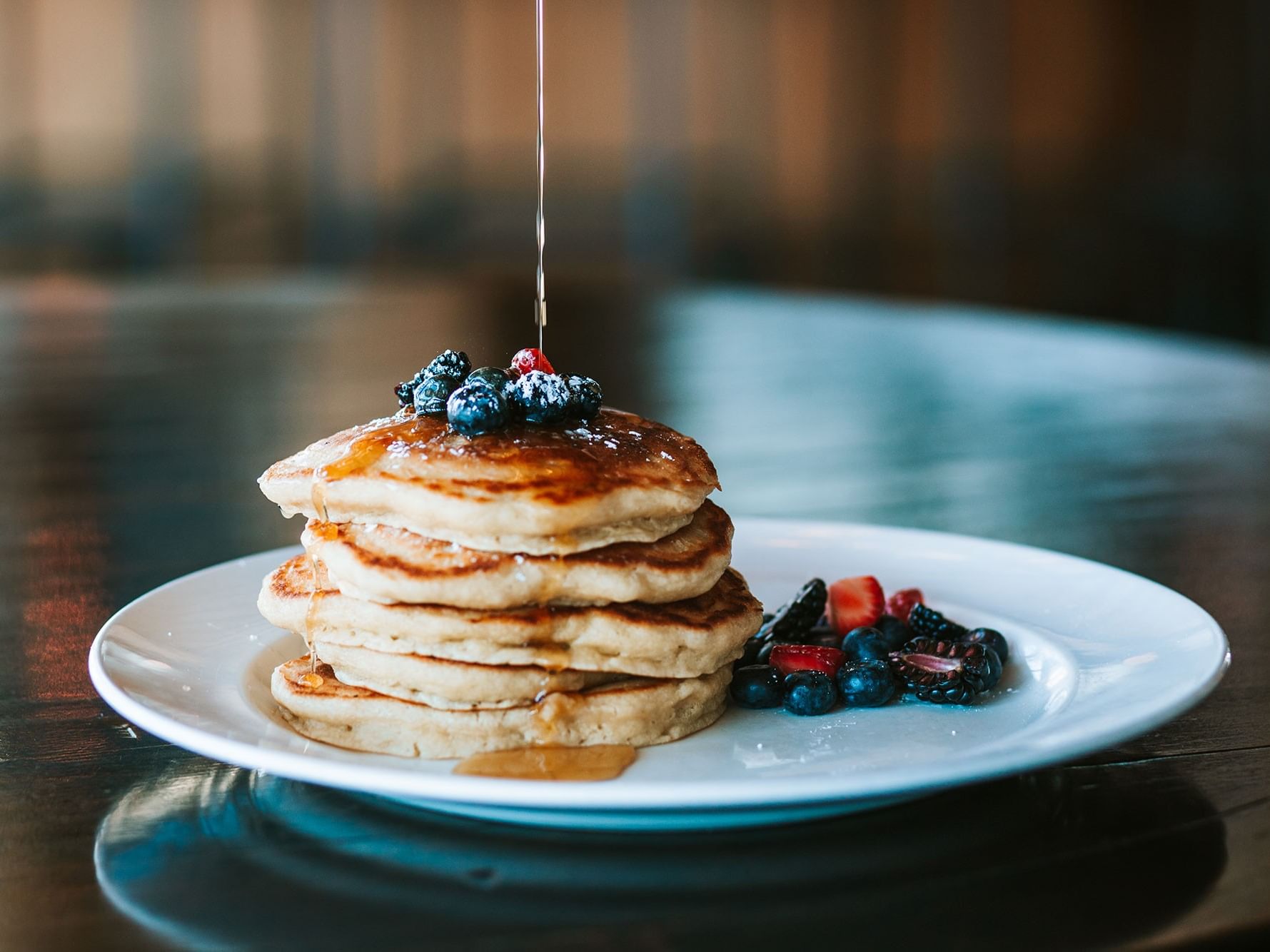 Stack of pancakes with berries and maple syrup being poured on top.