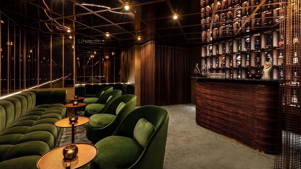Interior of a bar area with green couches & tables at The Londoner Hotel