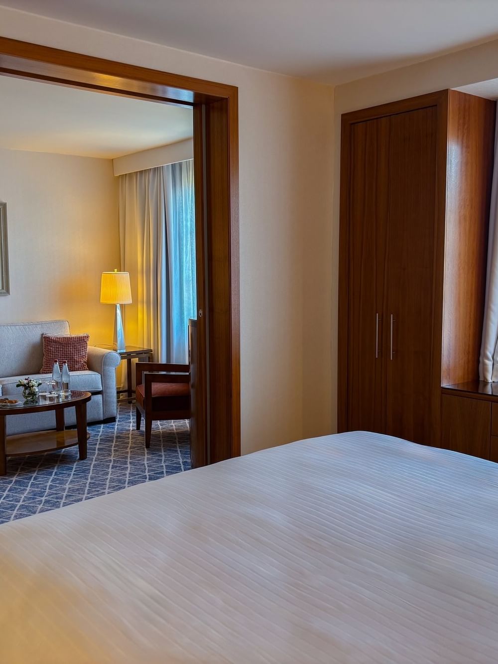 Bed facing a separate living area with a sofa through a wooden partition in Warwick Suite at Warwick Grand-Place Brussels