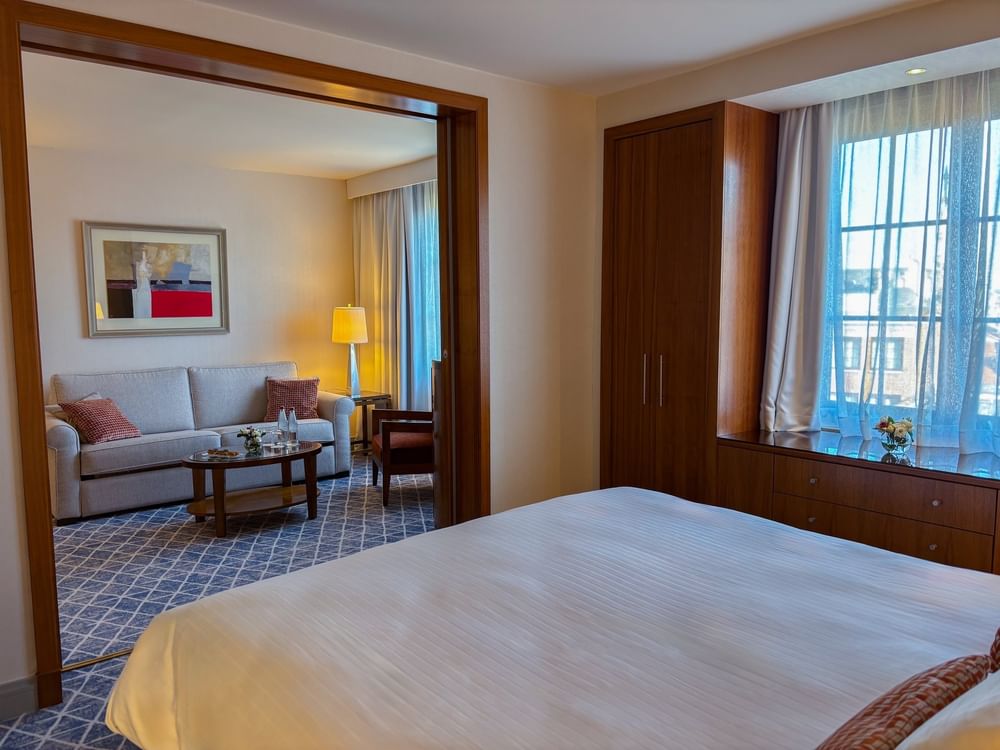 Bed facing a separate living area with a sofa through a wooden partition in Warwick Suite at Warwick Grand Place Brussels
