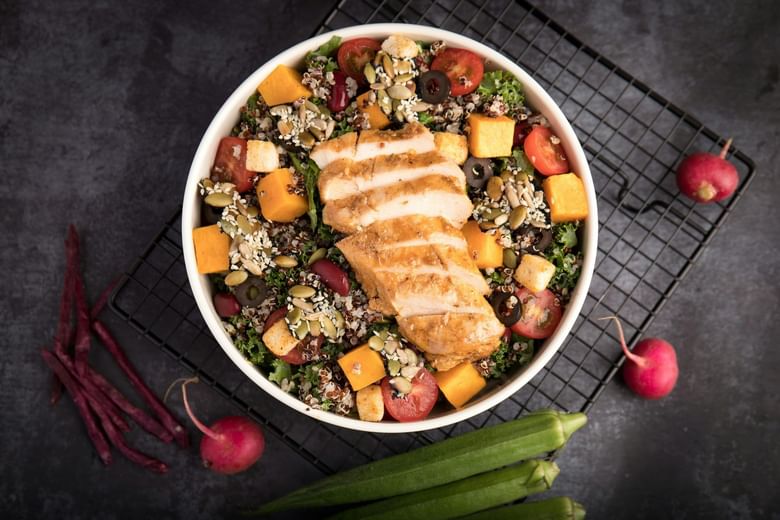 A bowl of salad with chicken, vegetables, and seeds.