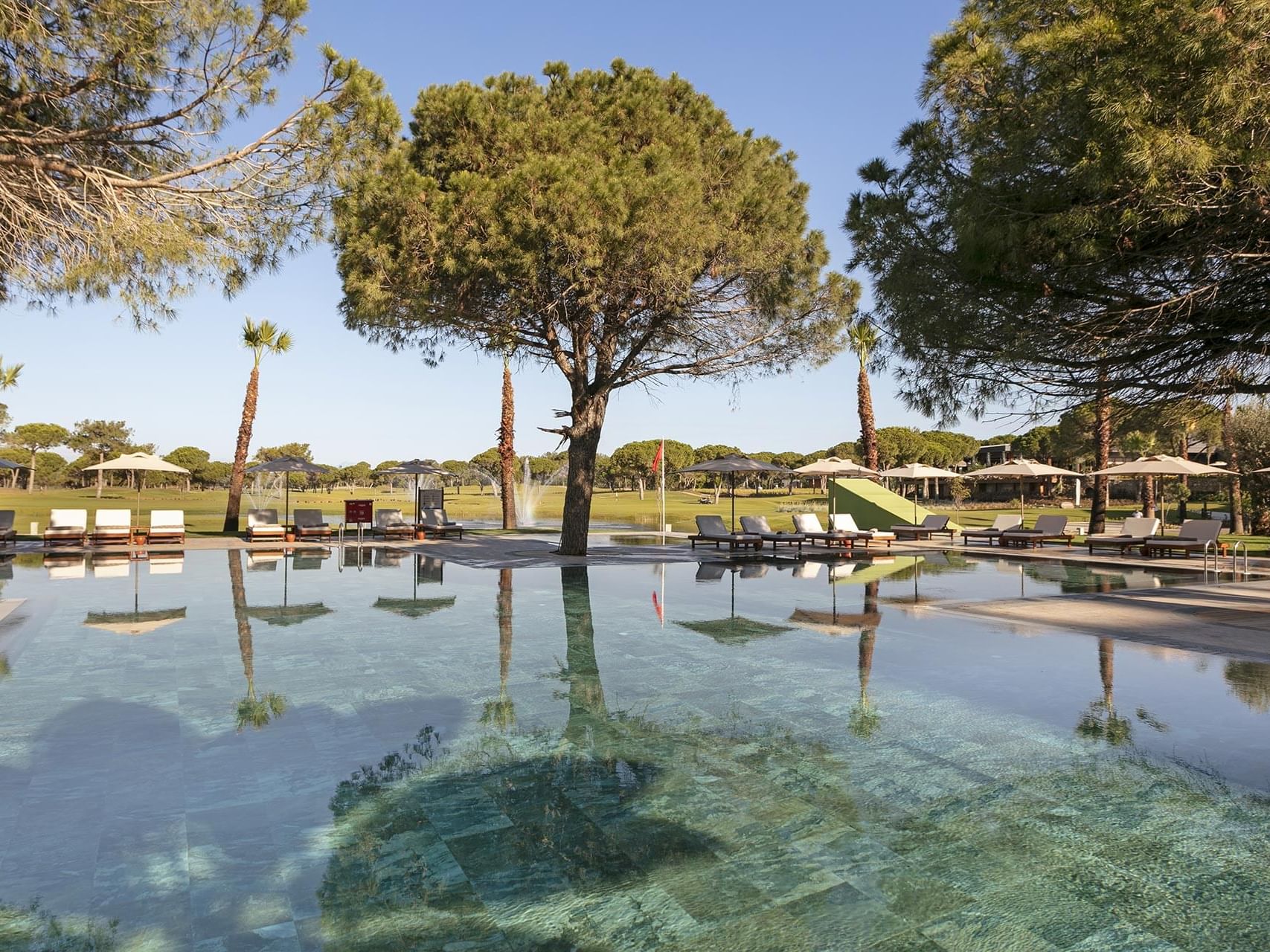 Sun loungers & patio umbrellas by Azure Pool with greenery in Cullinan Belek