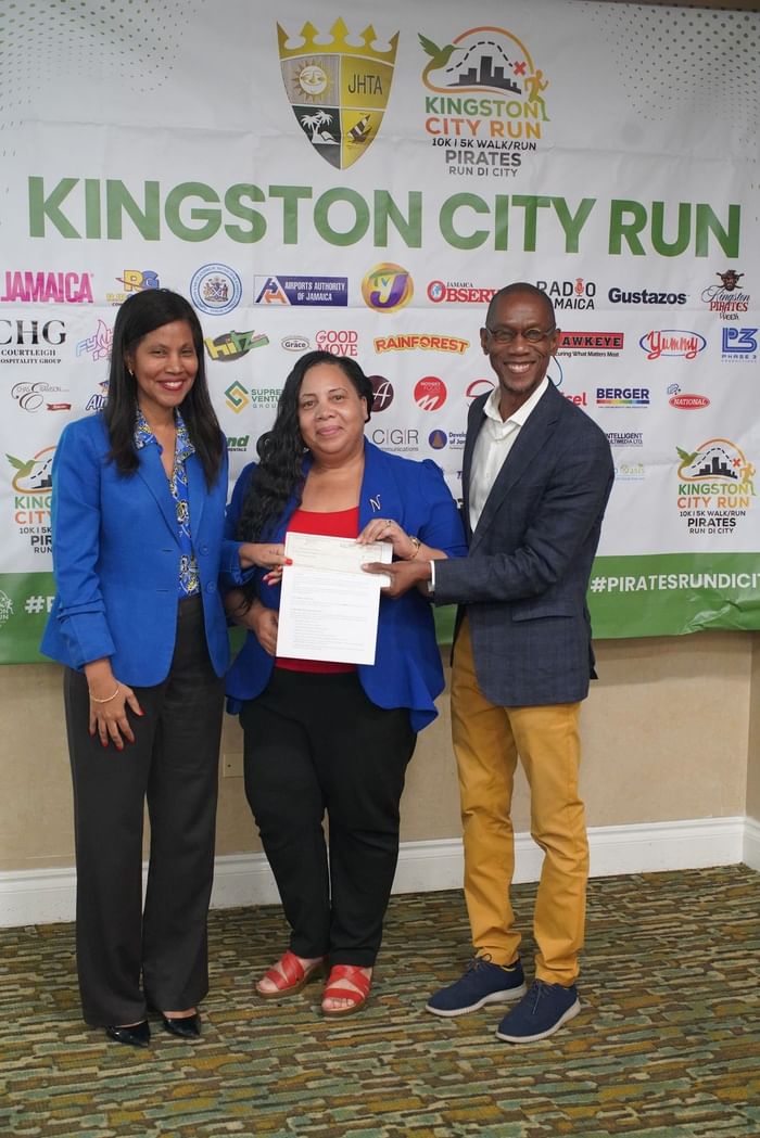 Three people holding a sponsorship check by the Kingston City Run banner at Courtleigh Hotel & Suites