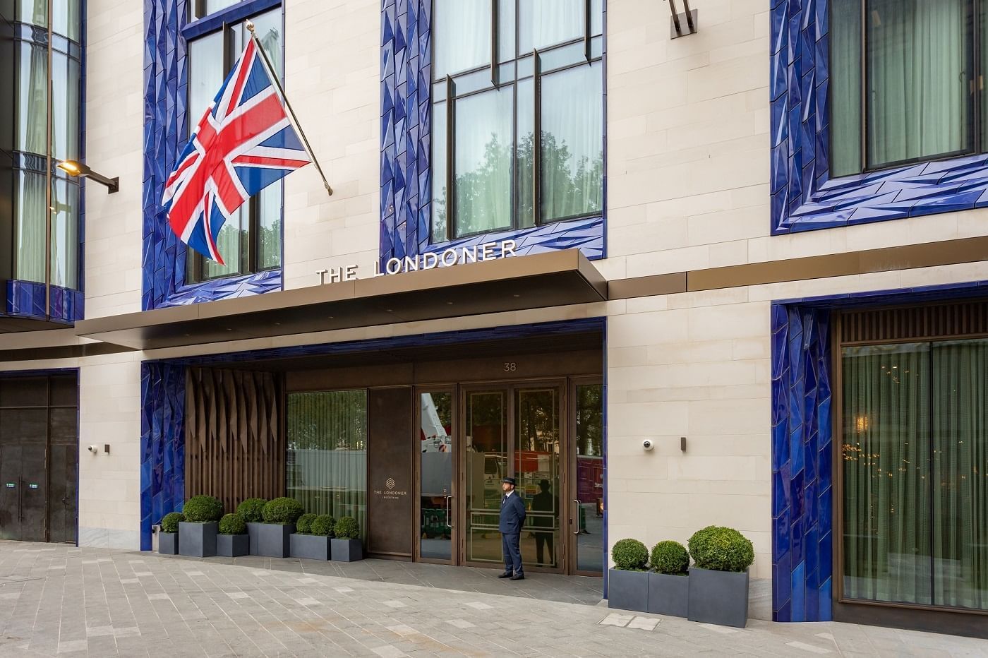 Exterior view of The Londoner Hotel’s grand entrance, with a Union Jack flag and an attentive doorman