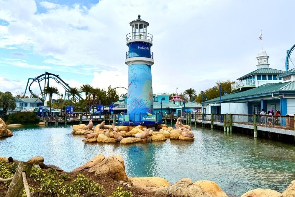 A blue lighthouse with a sign reading SeaWorld Orlando surrounded by statues of sea lions and walruses at the entrance to SeaWorld Orlando.