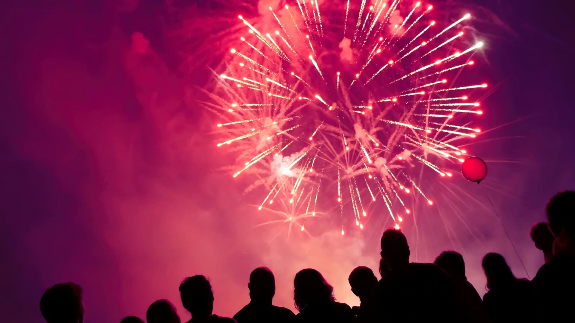 Crowd in silhouette watches a large pink and white firework burst in the night sky at Shangri-La Resort and Golf Club