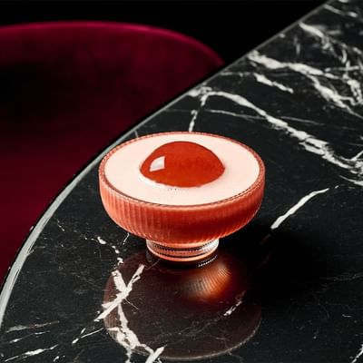 A cocktail with red and white layers in a short glass on a marble surface.