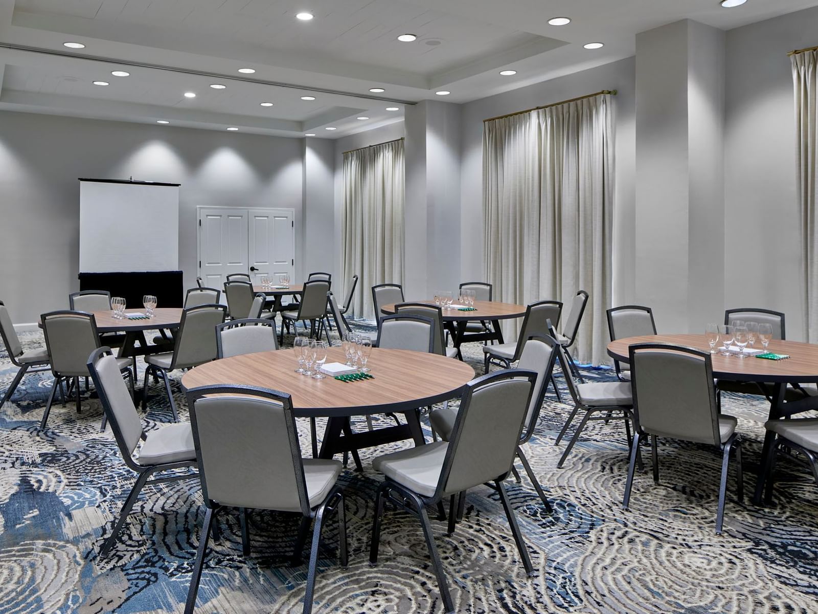 Sabal Ballroom with round tables, chairs, and a screen in front, on the blue carpet at the Inn at Celebration