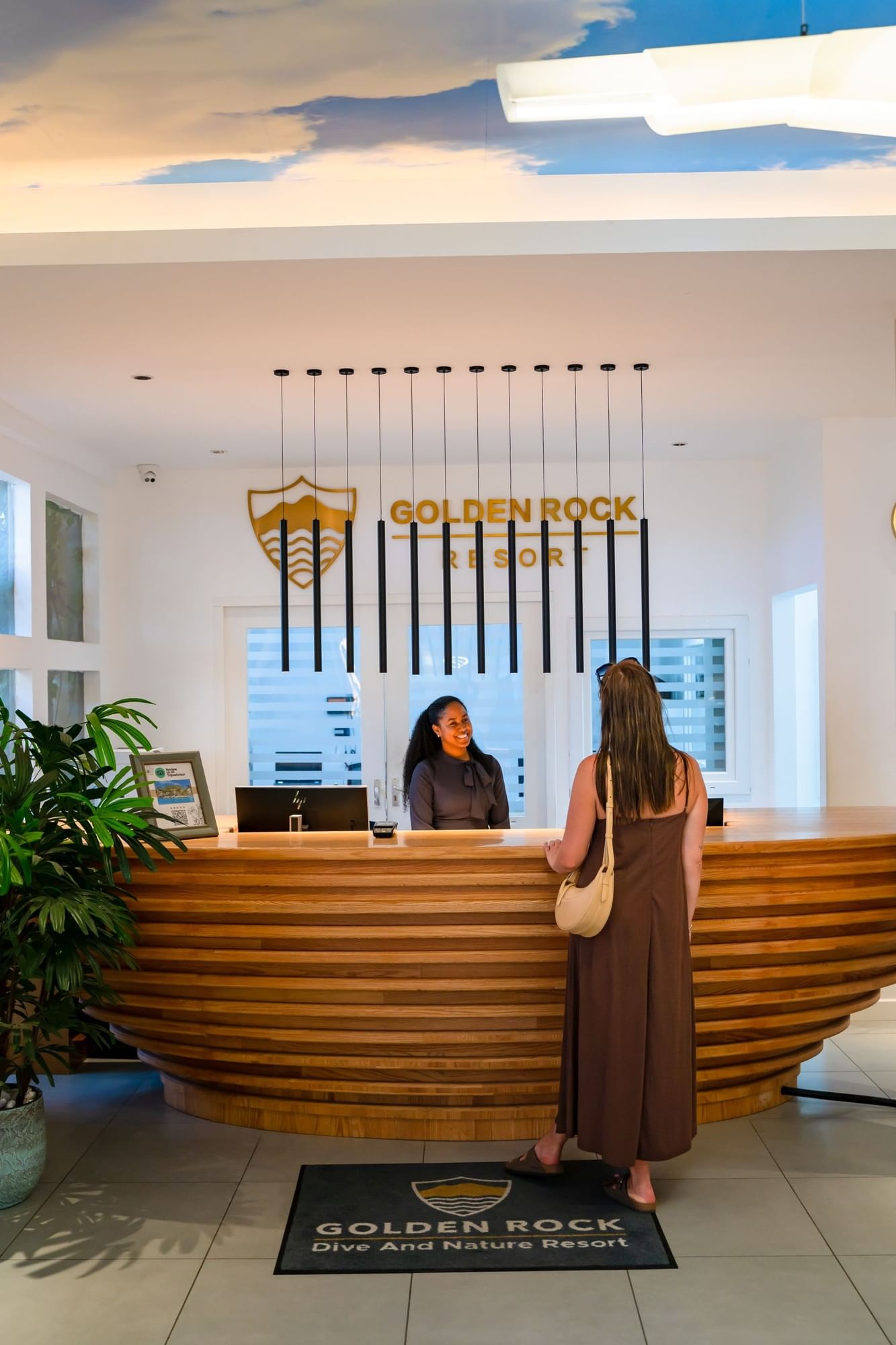 Guest checking in at wooden front desk with pendant lighting in bright reception lobby at Golden Rock Resort