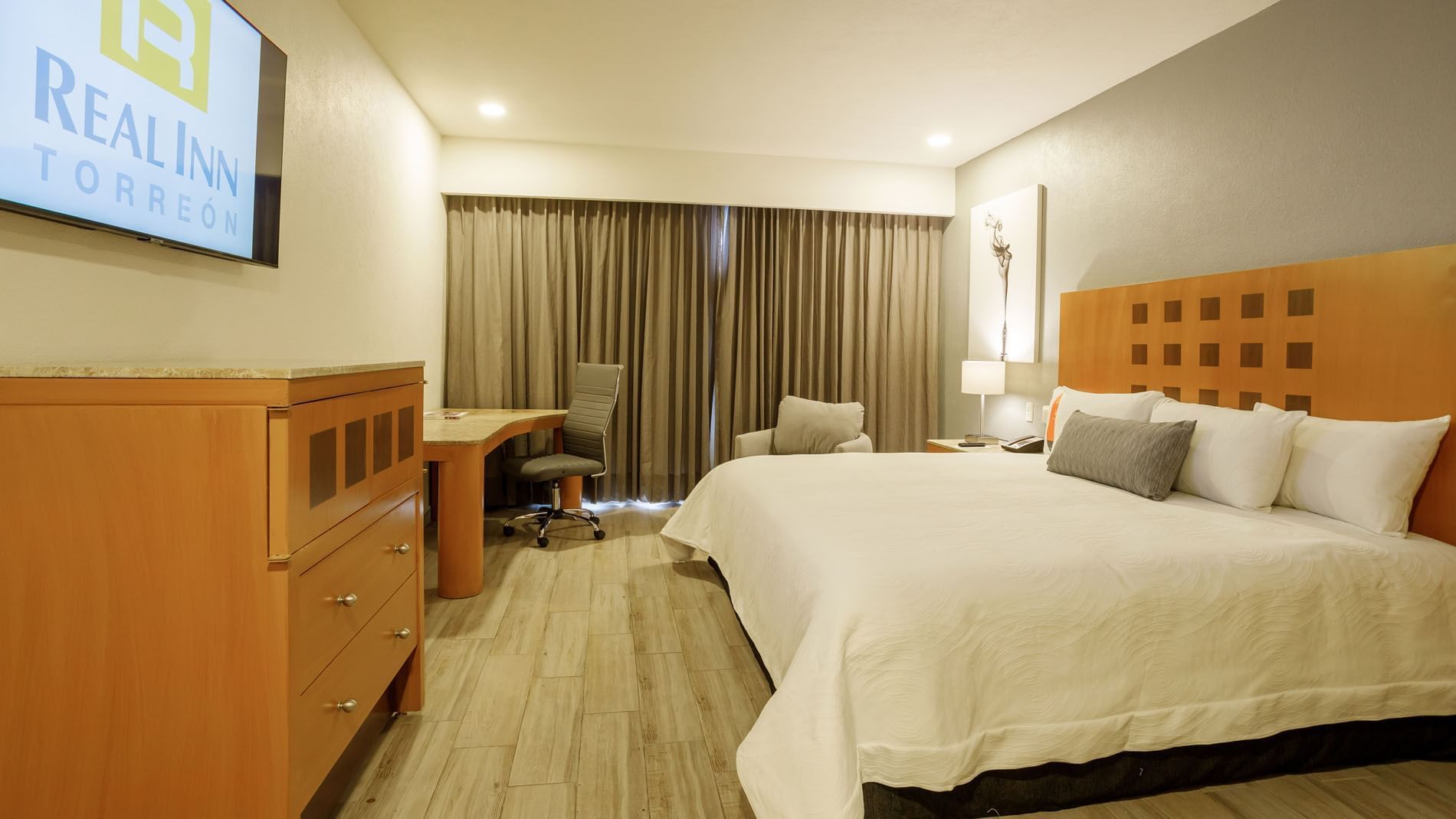 King Deluxe Superior room with heavy curtains, a wooden dresser, and a comfortable desk chair at Real Inn Torreon