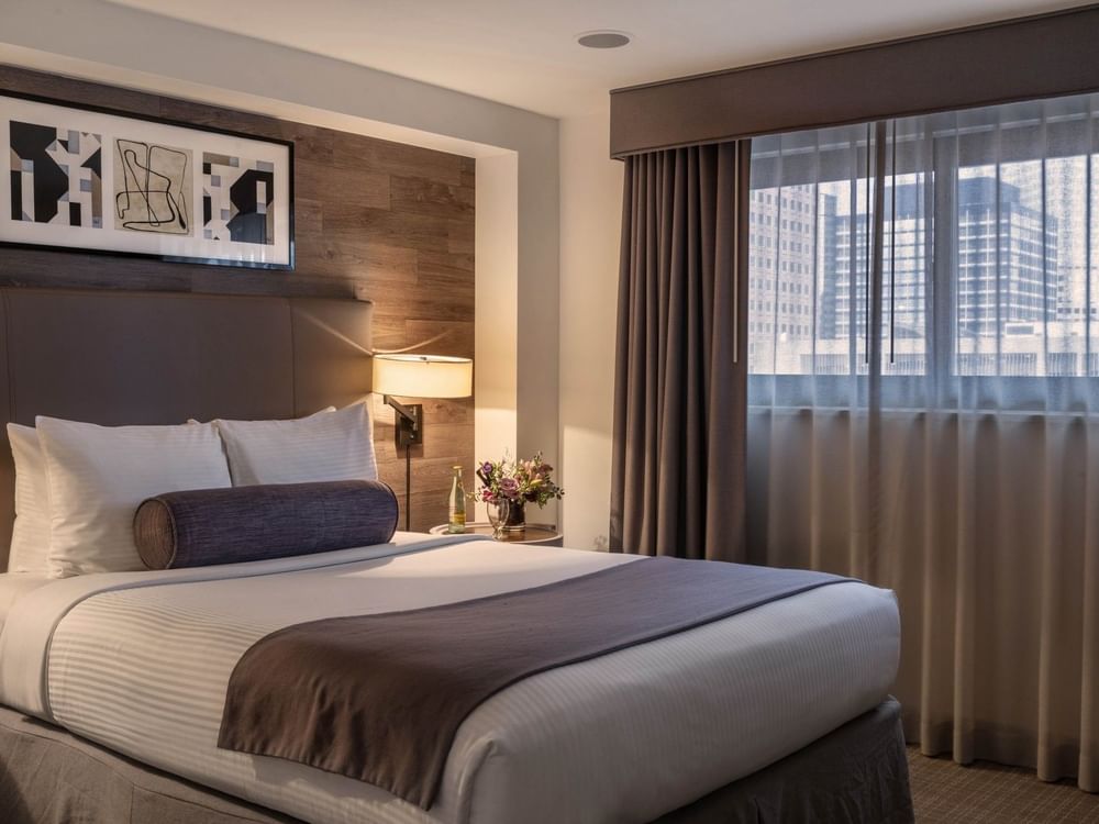 King bed with a purple bolster by a city view window under framed art in Premier Junior Suites at Warwick Denver