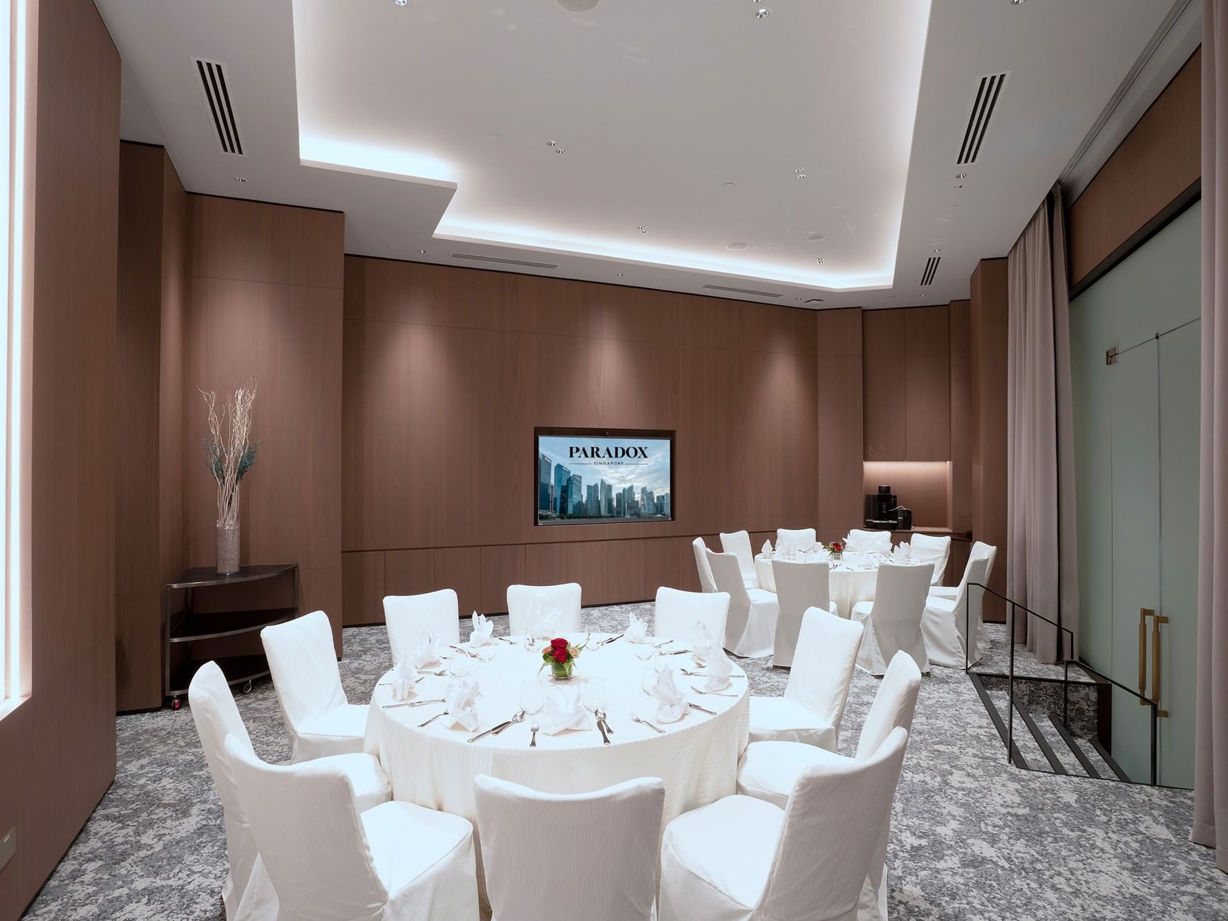 Round table banquet setting at Paradox Singapore, featuring elegantly dressed tables with white linens, neatly arranged place settings, glassware, and floral centerpieces in a well-lit meeting room.