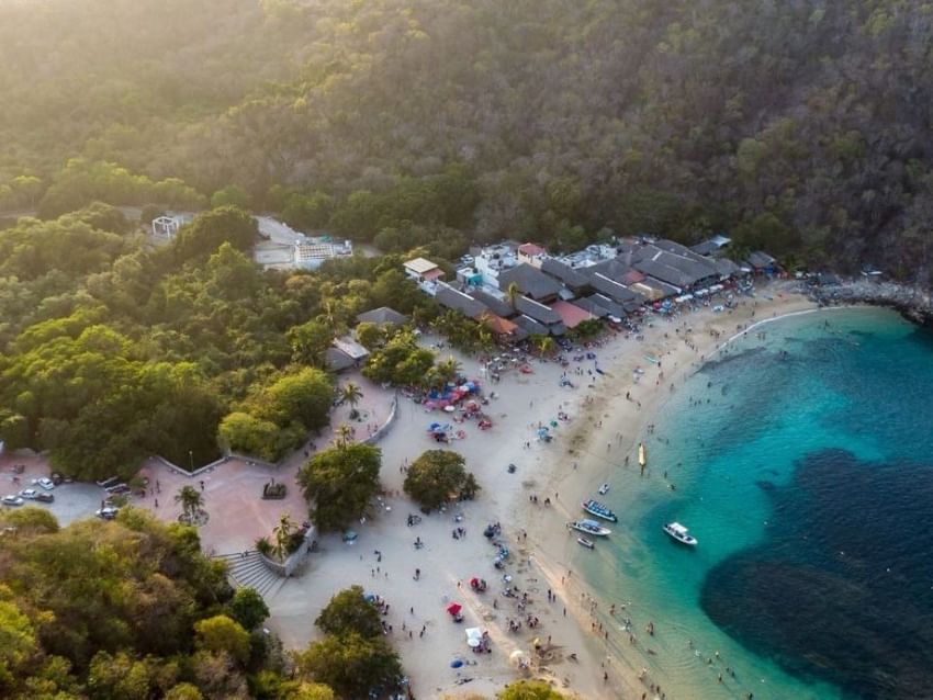 Vista aérea de playa tropical concurrida con agua turquesa y colinas verdes cerca de Camino Real