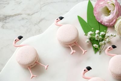 Plate of pink flamingo-themed macarons, surrounded by green leaves and delicate flowers at Park Hyatt Saigon