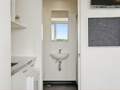 White bathroom with sink, mirror, and bulletin board at Student Living Auckland Anzac.