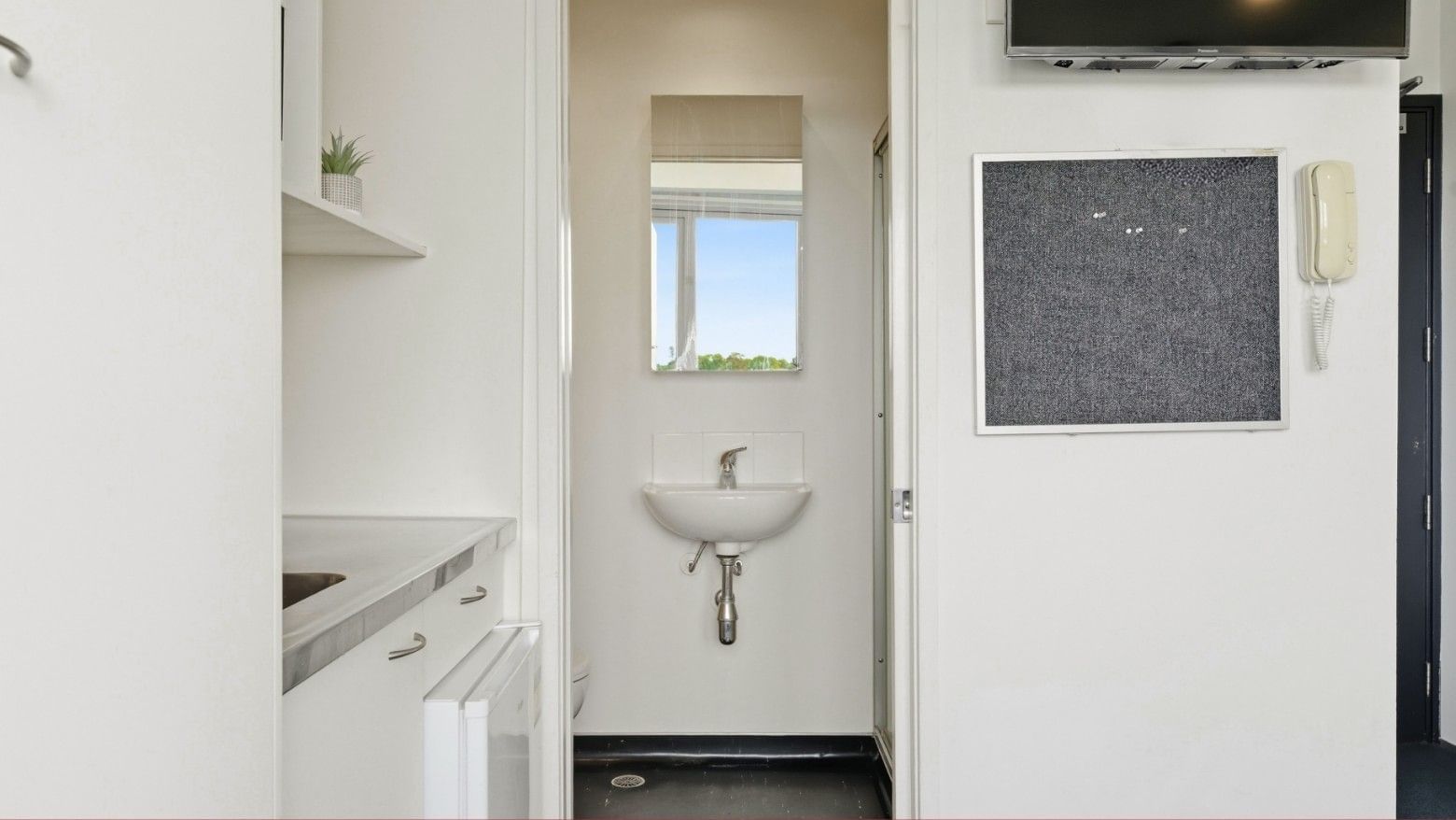White bathroom with sink, mirror, and bulletin board at Student Living Auckland Anzac.
