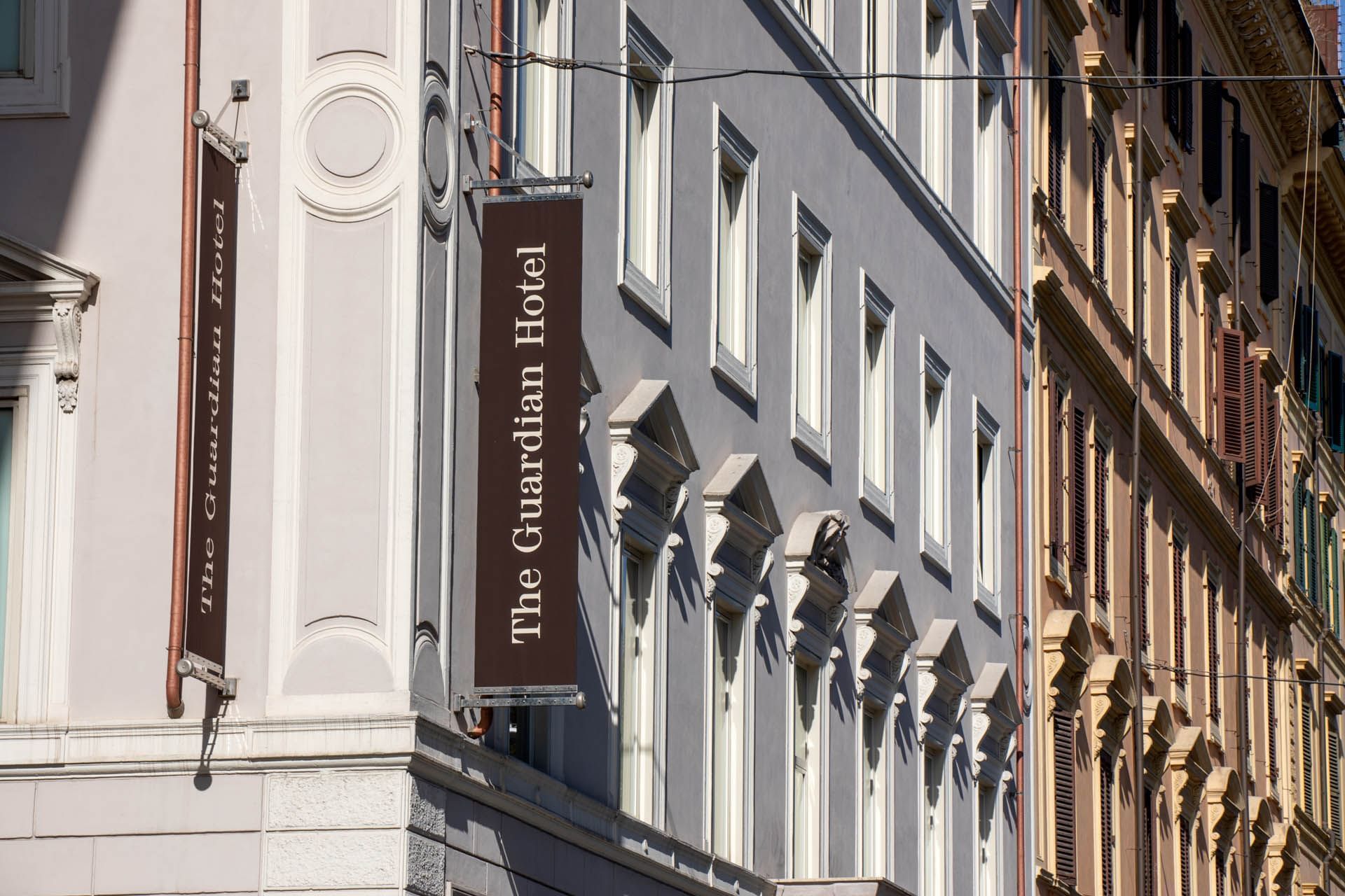 Close-up of The Guardian Hotel exterior with elegant architecture and two signs on a sunny day