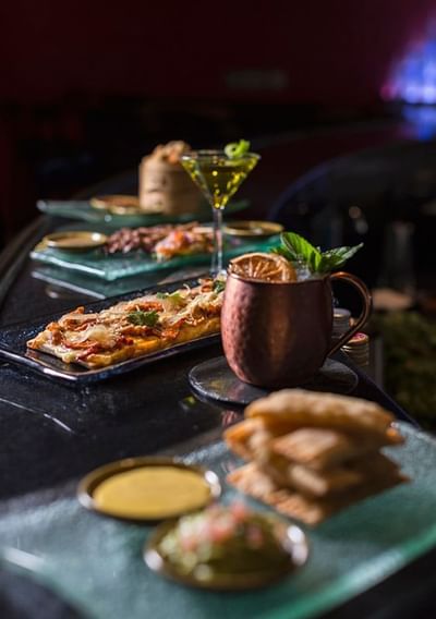 Gourmet flatbread, cocktails, and appetizers arranged on plates in Oceanus Lounge at Hotel Los Delfines & Casino