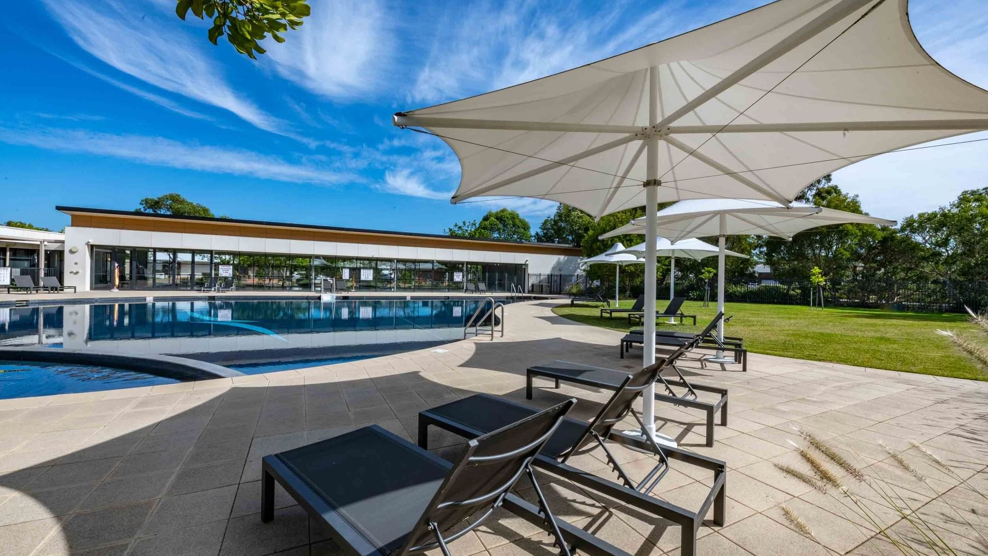 Outdoor pool with sun loungers and white parasols at Mercure Kooindah Waters