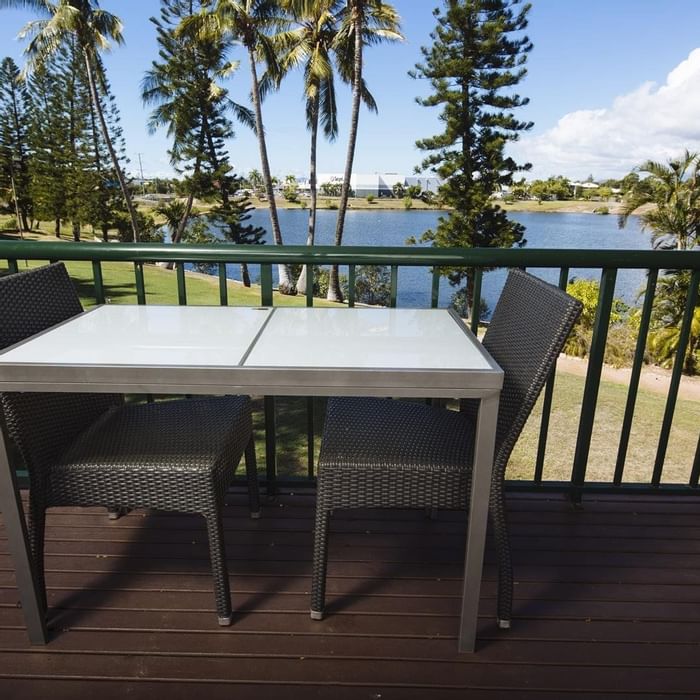 Balcony with a table with woven chairs overlooks a lake surrounded by trees at Mercure Hotel Townsville