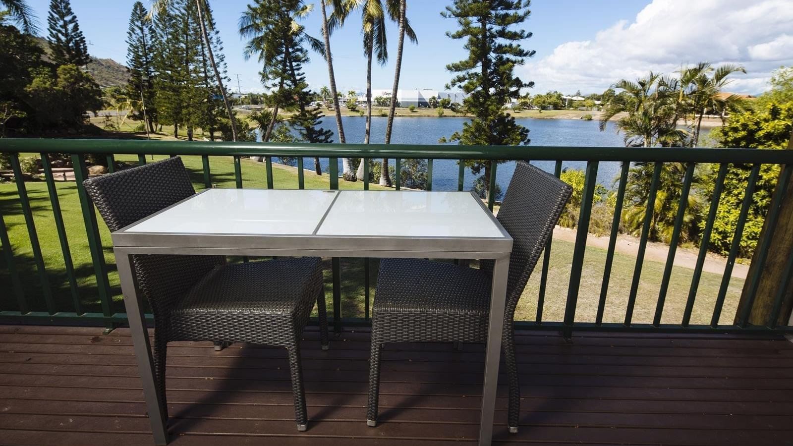 Balcony with a table with woven chairs overlooks a lake surrounded by trees at Mercure Hotel Townsville