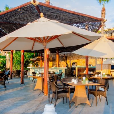 Patio exterior del restaurante Tortugas en Hacienda del Mar Los Cabos con mesas, sillas y sombrillas grandes.