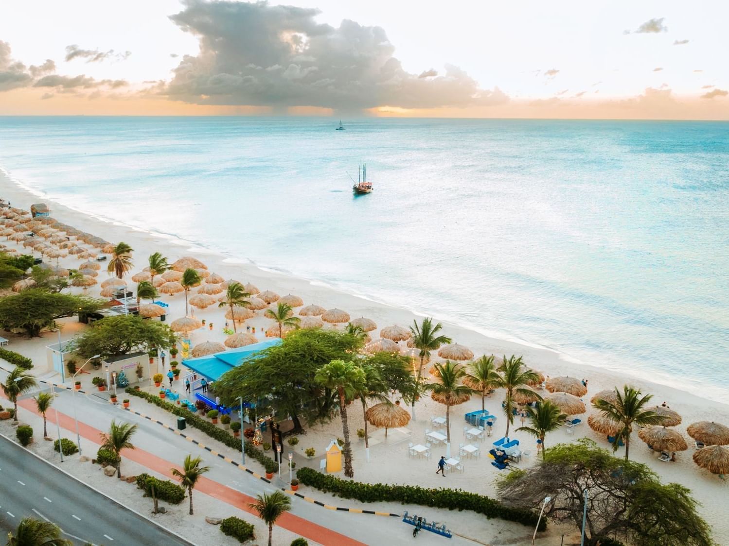 Aerial view of a white sand beach with palm trees and a boat at Amsterdam Manor Beach Resort