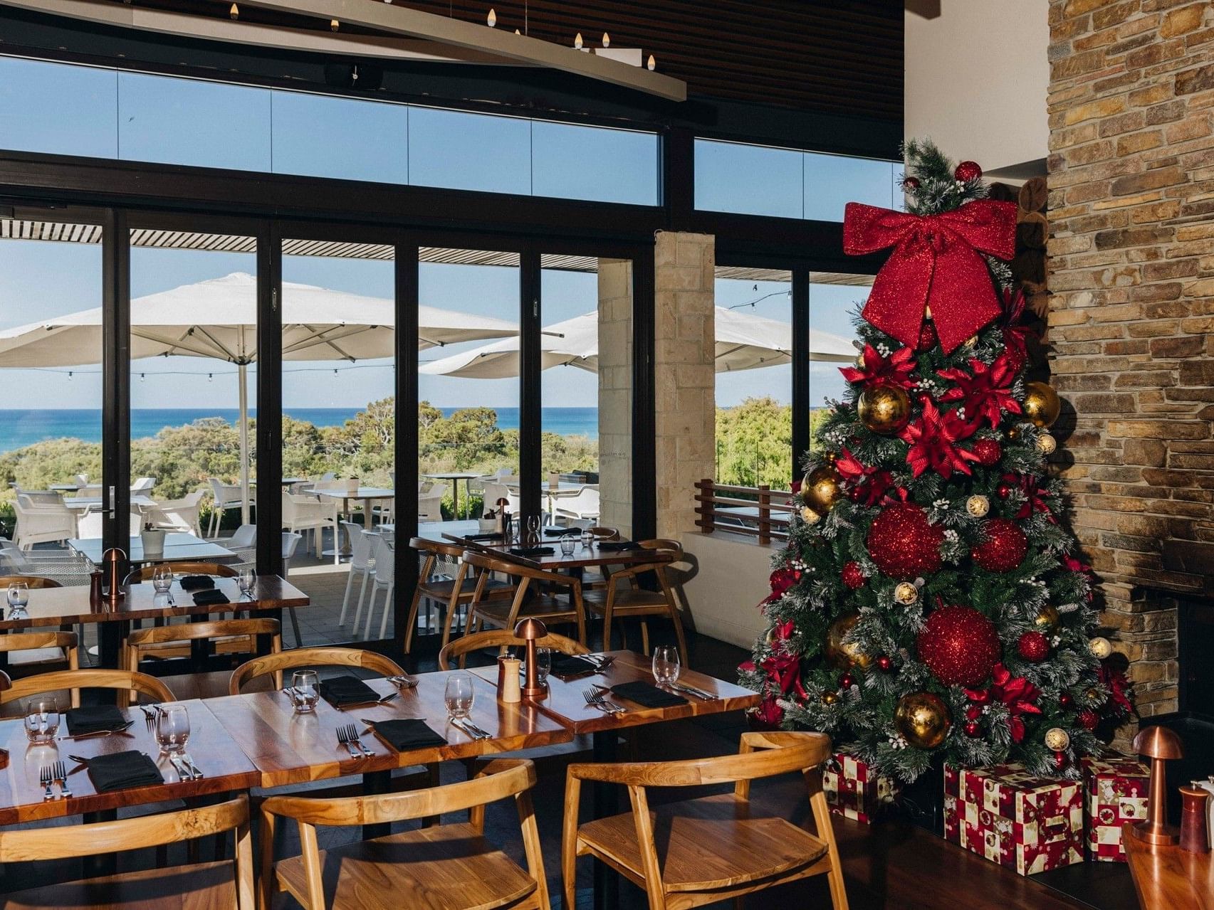 Restaurant dining area with decorated Christmas tree, ocean views through large windows, and festive table settings
