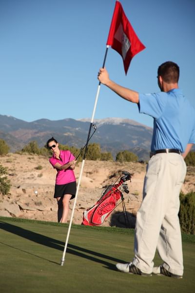 Woman golfer swinging as a man tends the pin at a Towa Golf Club course near Hilton Santa Fe Buffalo Thunder