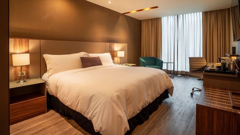 King Deluxe room with king bed, teal armchair, desk area and large window at Camino Real Fashion Drive, Monterrey