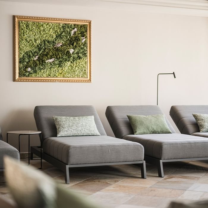 Three gray lounge chairs with pillows, a wall-mounted framed moss art piece, and a green floor lamp.