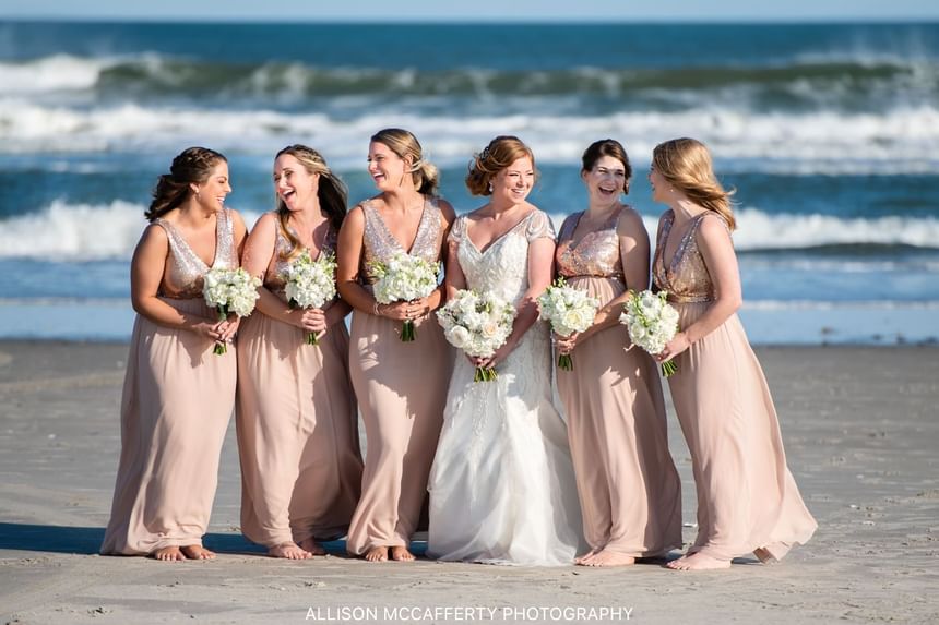 Bride with bridesmaids take a photo on the beach near our Avalon wedding venue