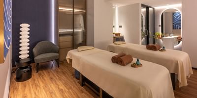A serene massage room with two treatment beds, cozy seating, soft lighting, and decorative accents at One World Hotel