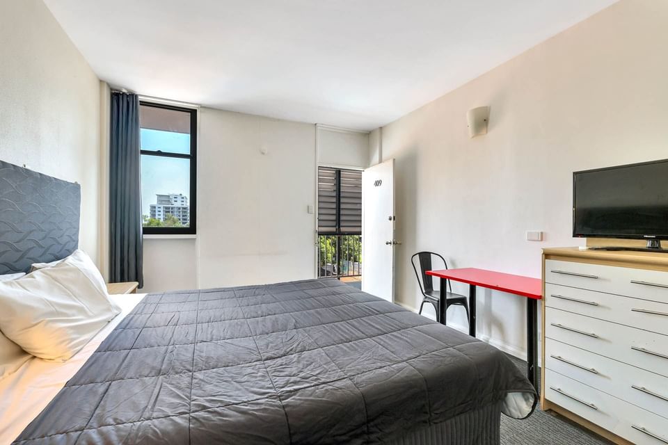 Bed facing TV and balcony area in King Room at Darwin Poinciana Inn