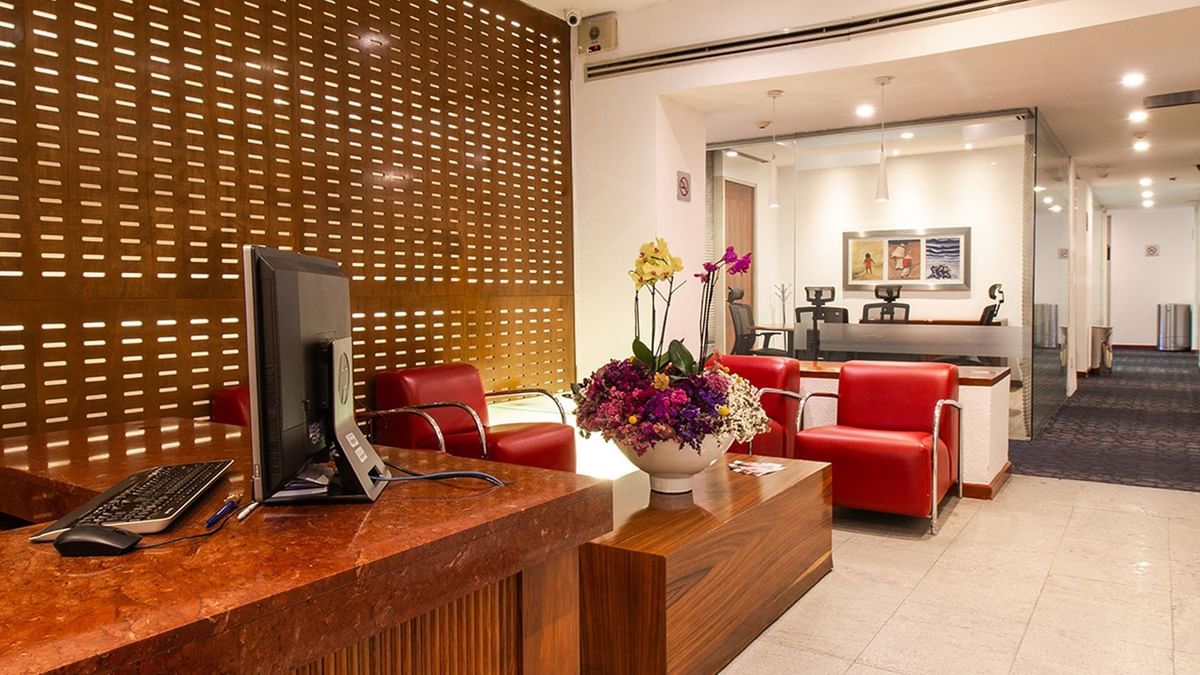 Reception area with a wooden desk, red armchairs, and a floral centerpiece at Camino Real Aeropuerto Mexico
