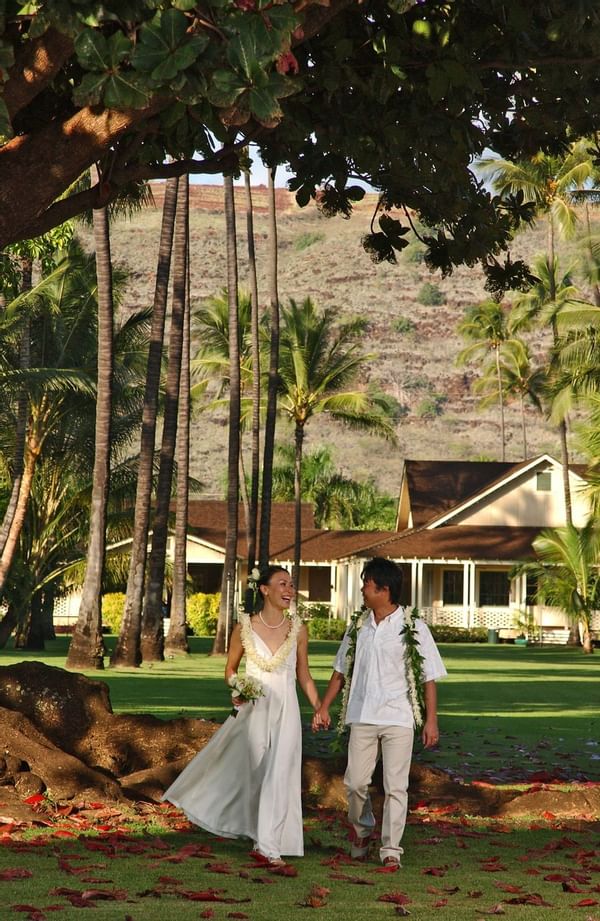 Bride and groom walking in grassy area surrounded by palm trees