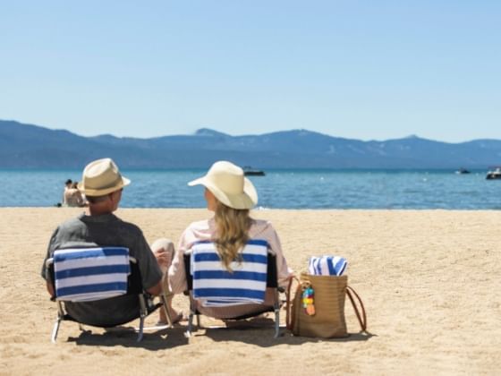 A couple lounges on the sands of a beach with mountains in the distance